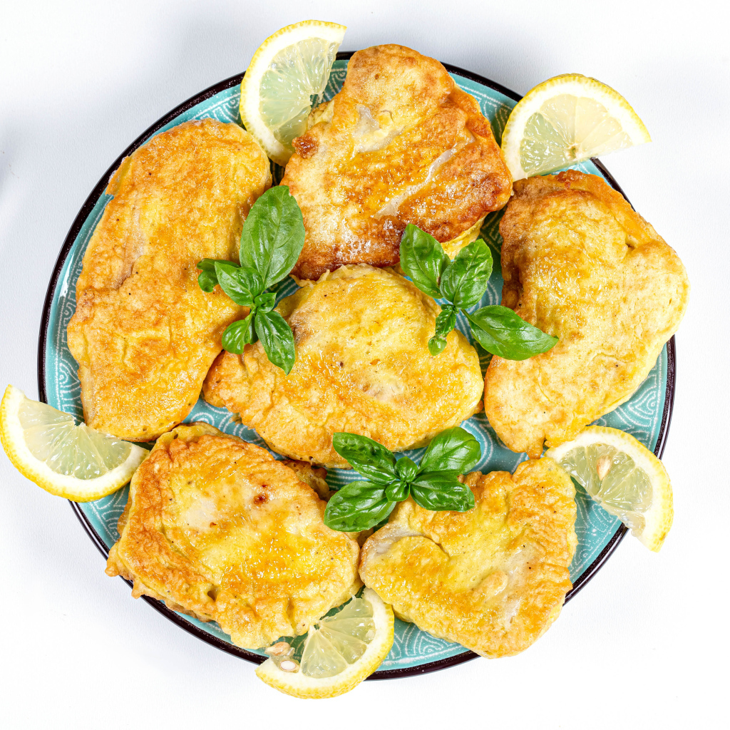 Аппетитная рыба в кляре на тарелке с кусочками лимона и столовыми приборами