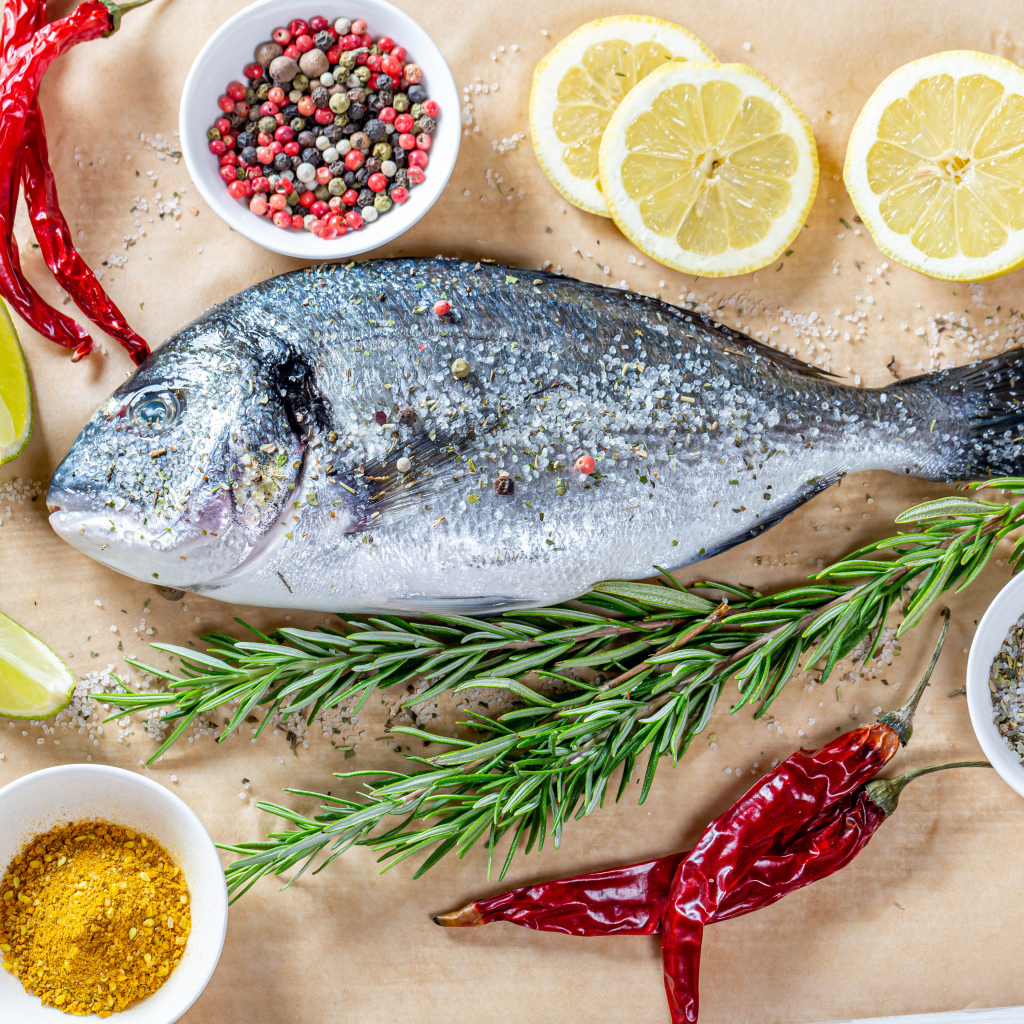 Fresh fish on the table with spices, lemon, rosemary and red pepper