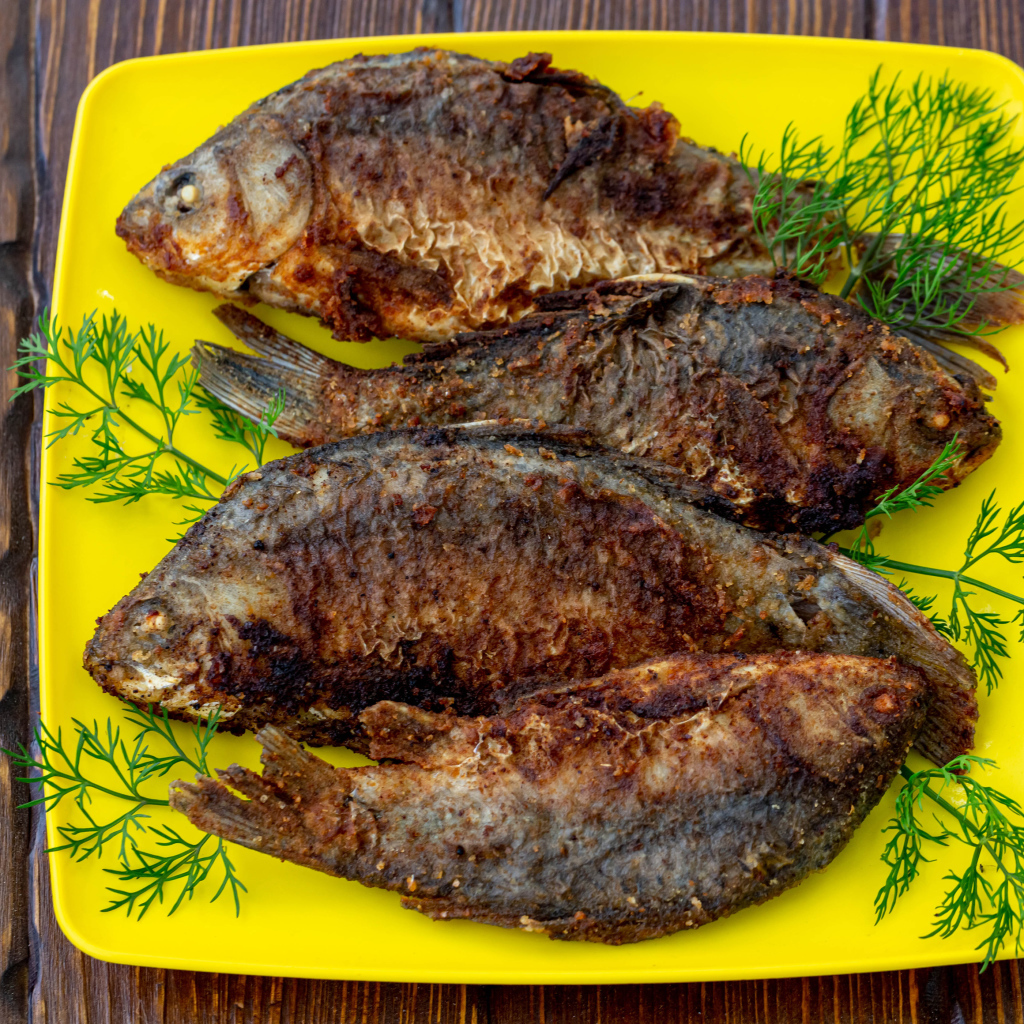 Жареные караси с укропом на желтой тарелке 