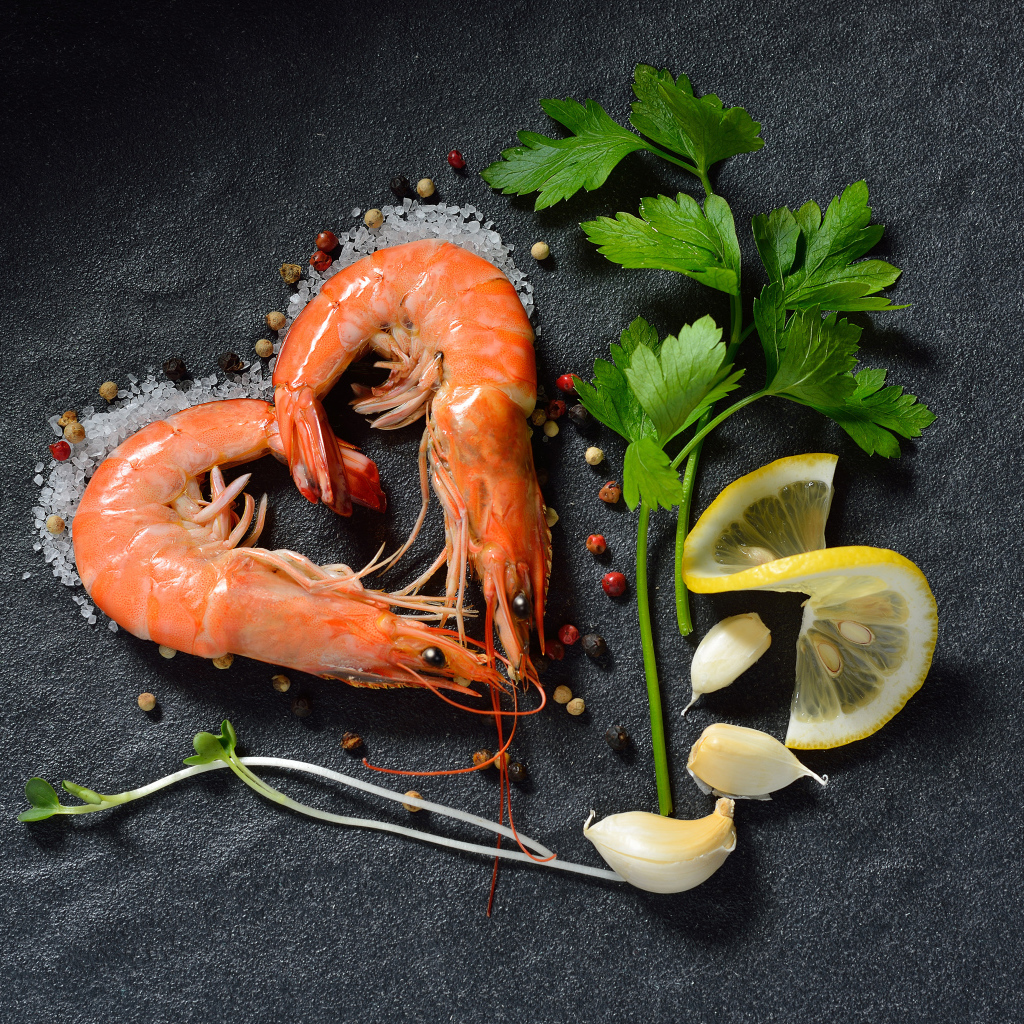 Сердце из креветок на сером столе с лимоном и веточкой петрушки 