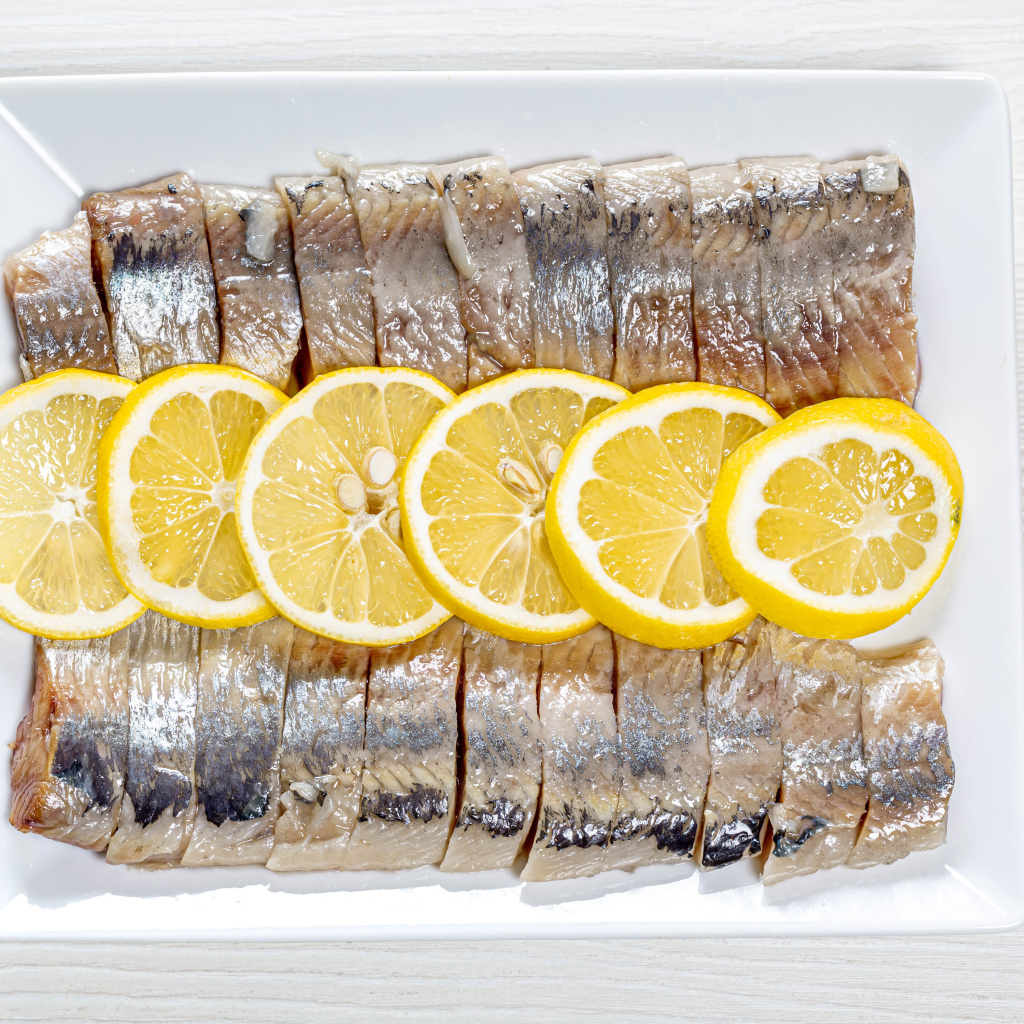 Селедка нарезанная кусочками на белой тарелке с лимоном 