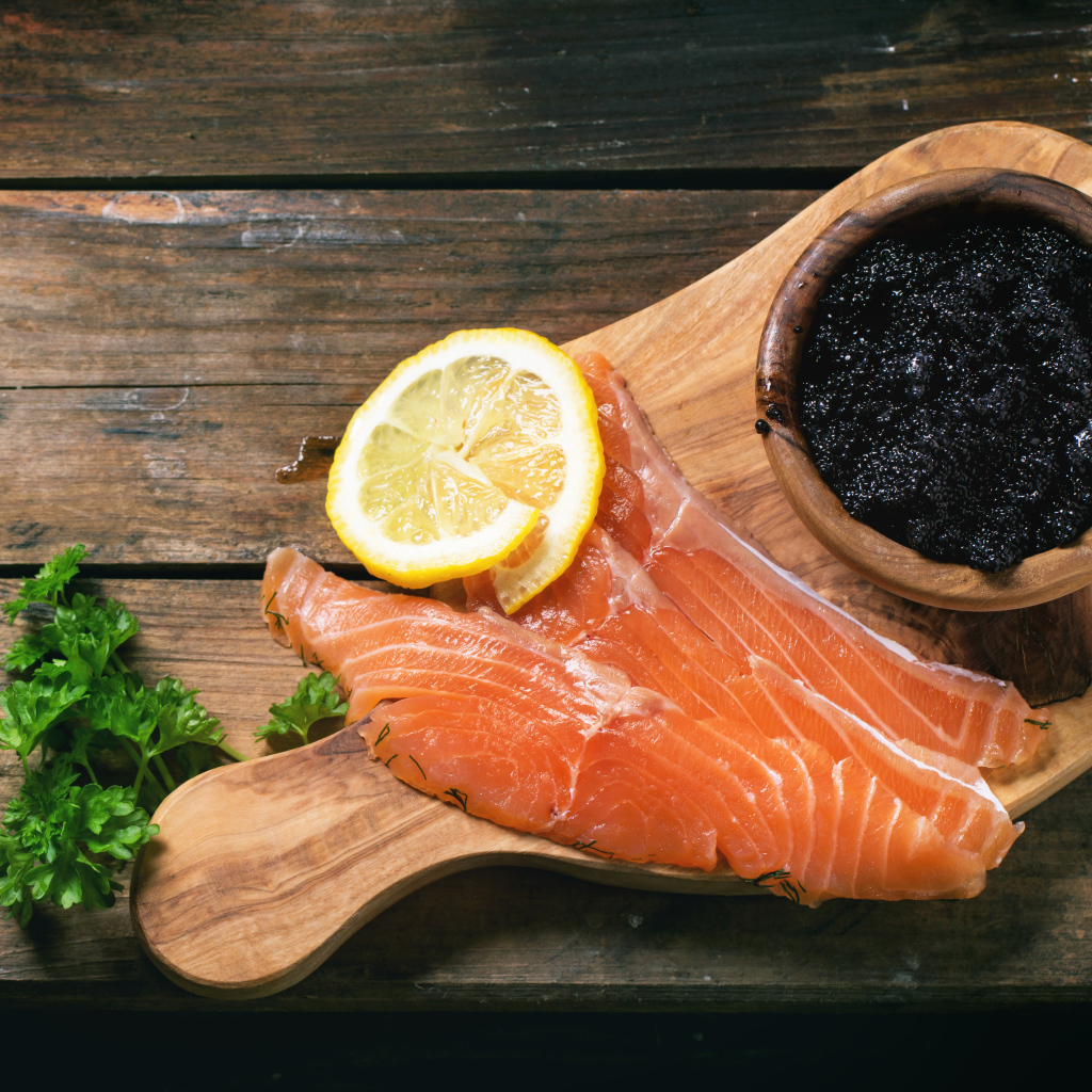 Slices of red fish with lemon on a table with black caviar