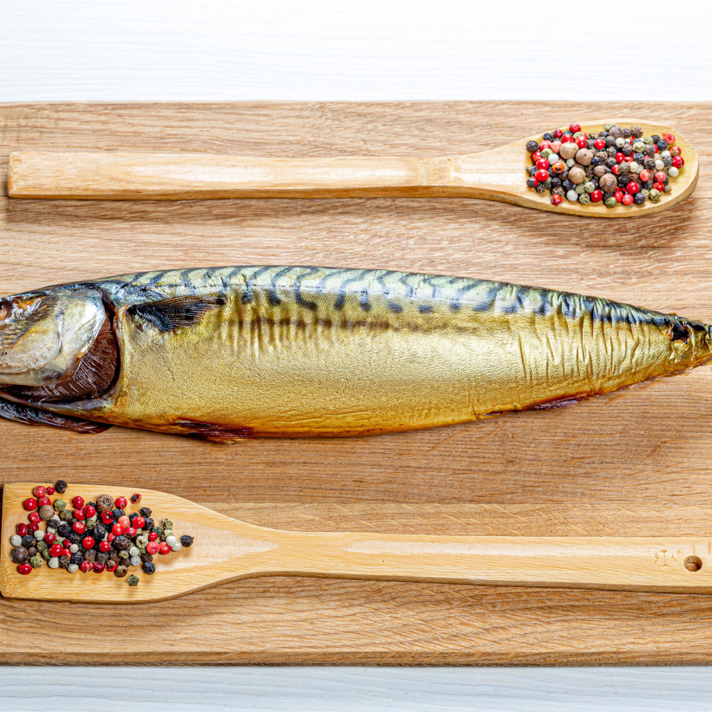 Копченая скумбрия на разделочной доске с перцем на белом фоне