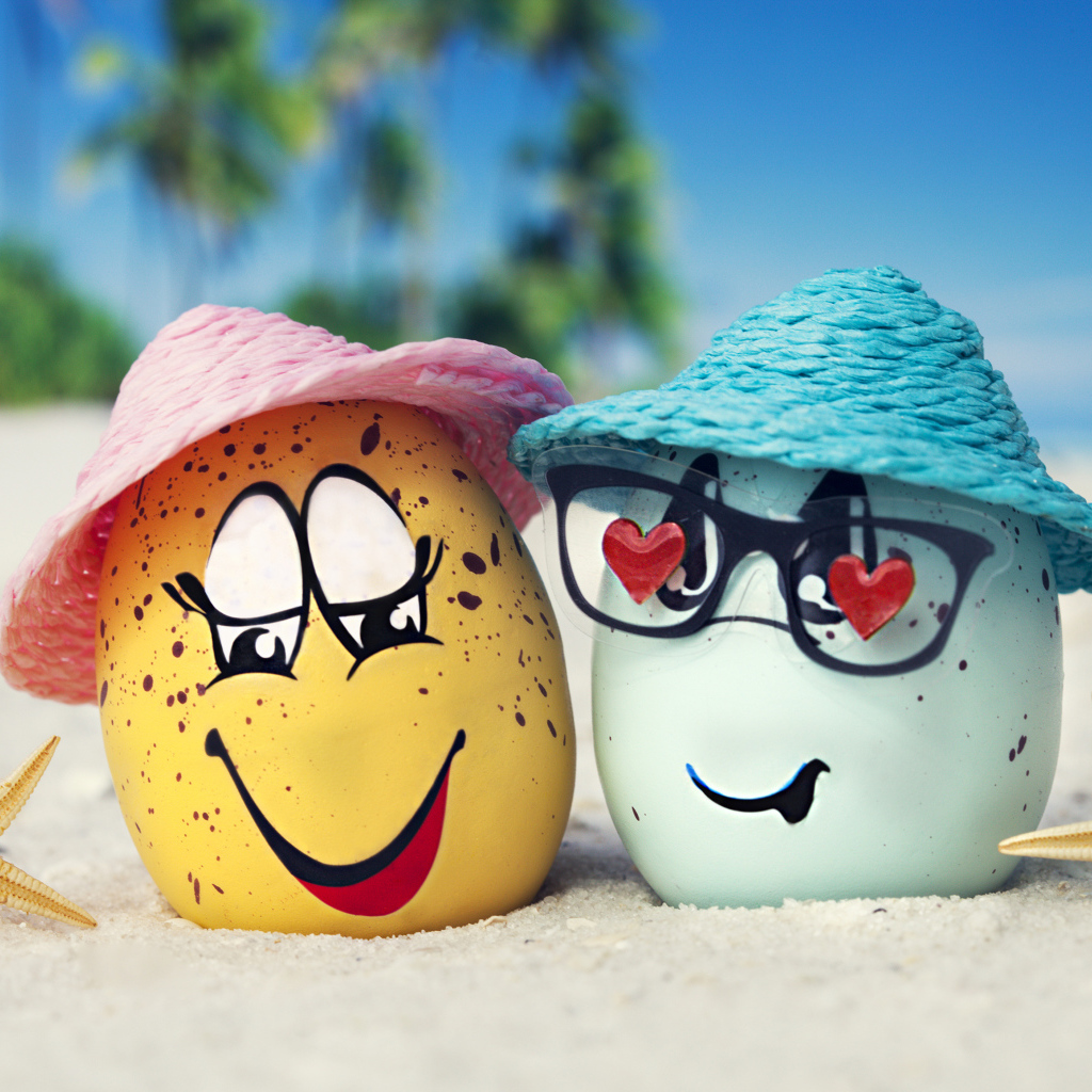 Два яйца в шляпах на песке с морскими звездами летом