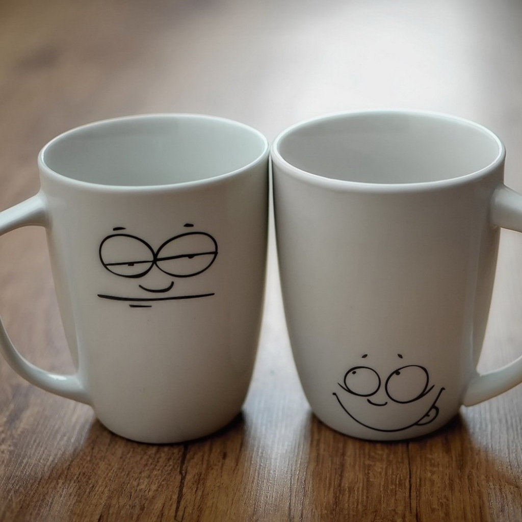 Две белые кружки с рисунками на столе 