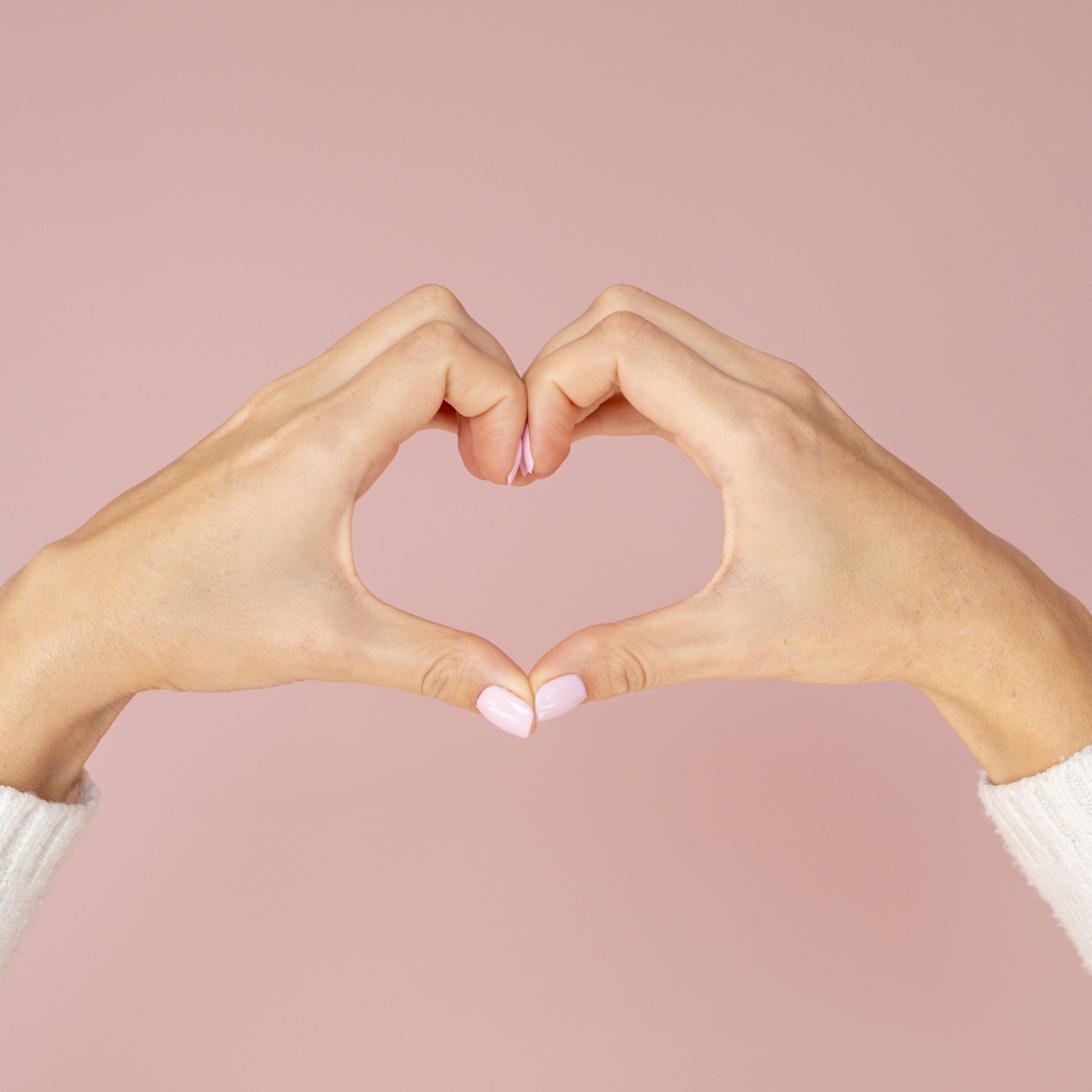Девушка делает сердце руками на розовом фоне 
