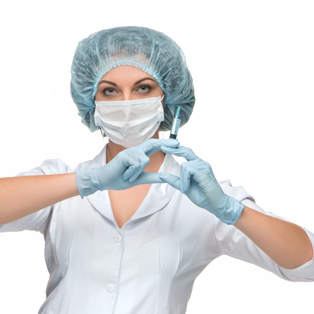 Девушка медсестра в маске со шприцем в руках на белом фоне