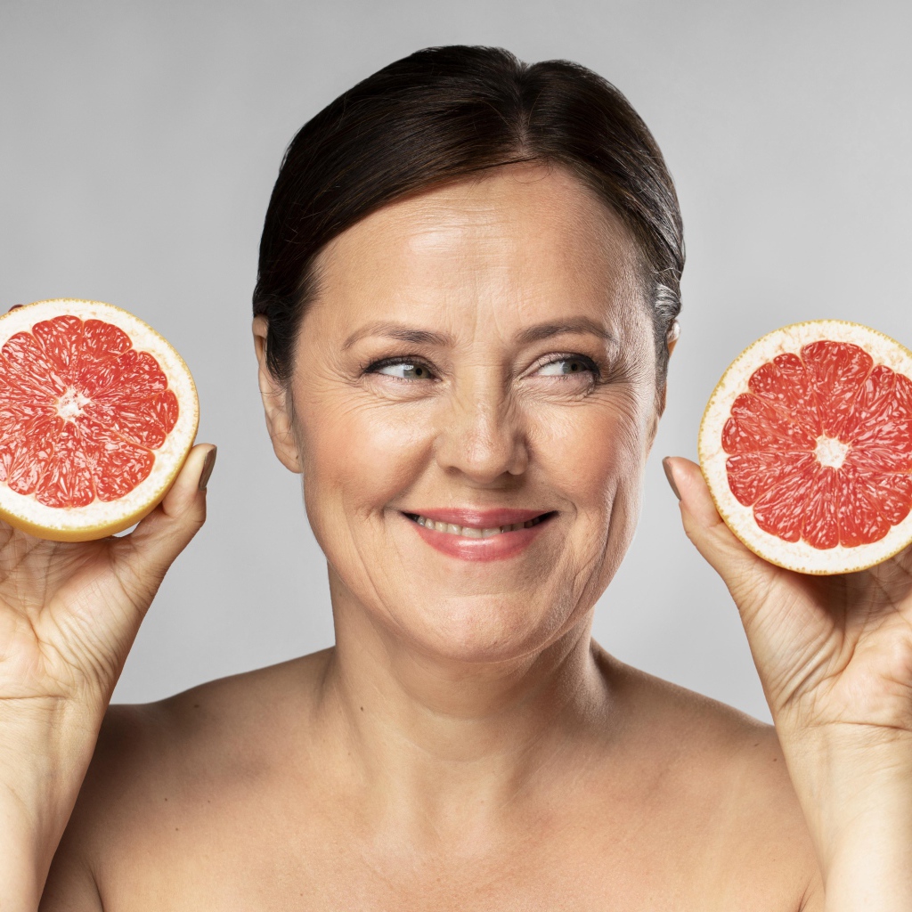 Smiling woman with grapefruit in hands on gray background