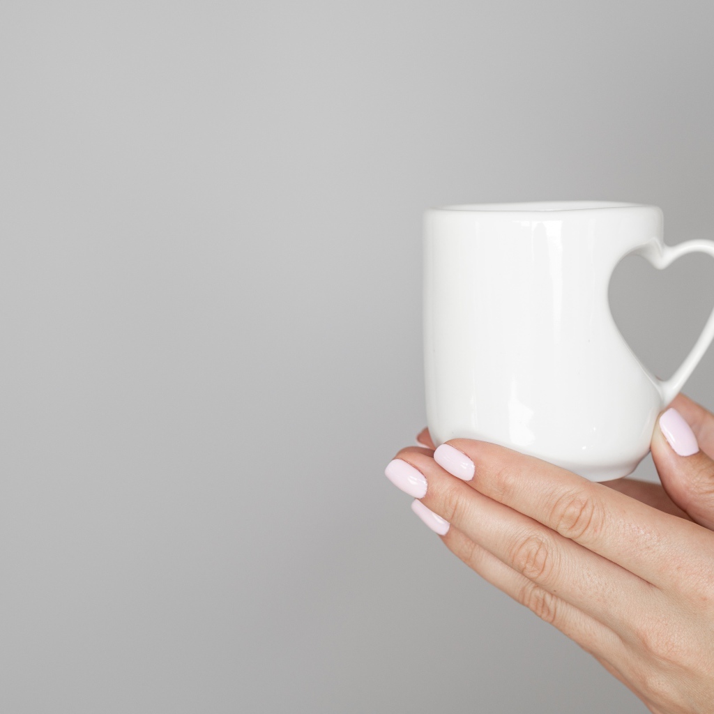 Белая кружка в руках девушки на сером фоне