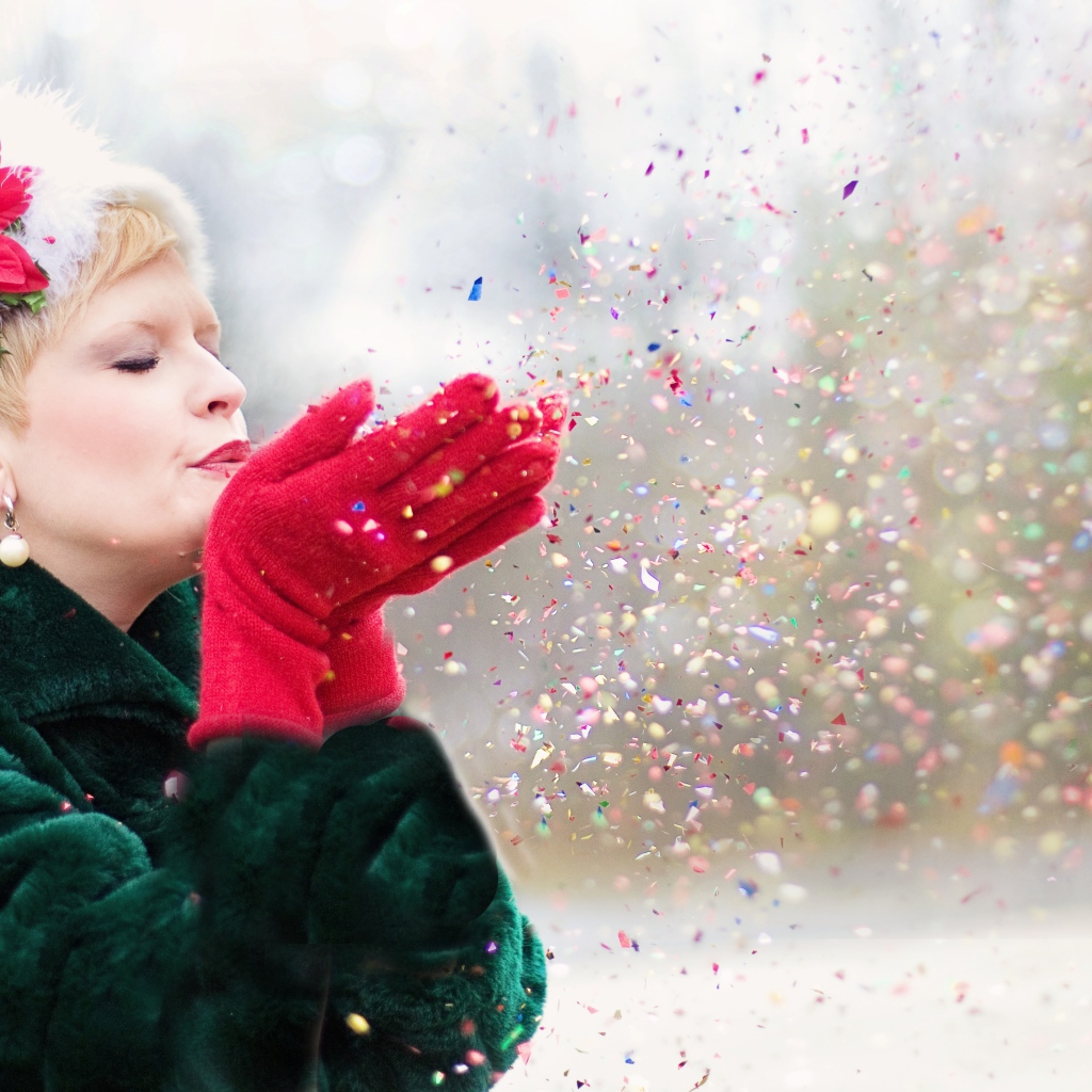 Женщина в шубе сдувает конфетти с ладоней