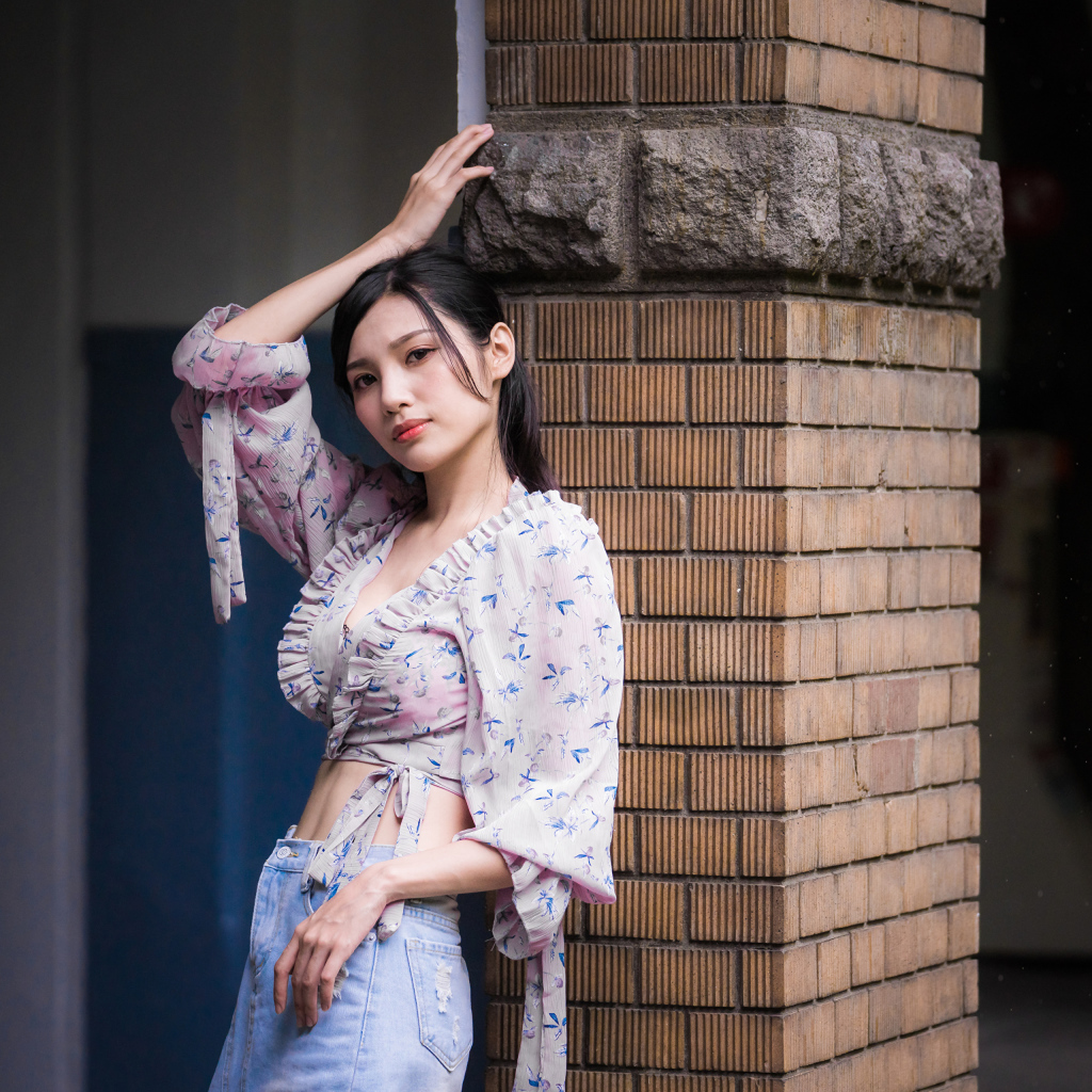 Красивая девушка азиатка стоит у кирпичной колонны 