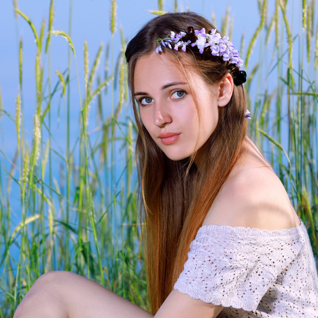 Красивая молодая девушка с венком на голове сидит на поле с колосьями 