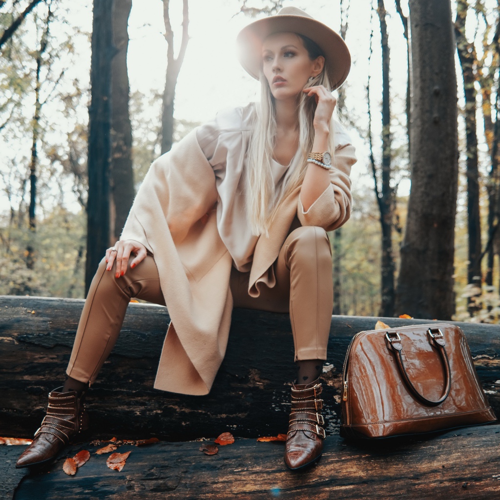 Девушка в пальто сидит на упавшем дереве в лесу 