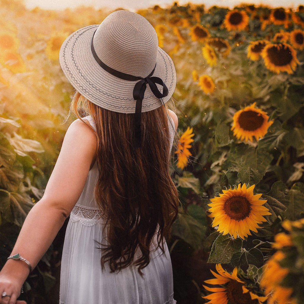 Девушка в белом платье и шляпе гуляет по полю с подсолнухами
