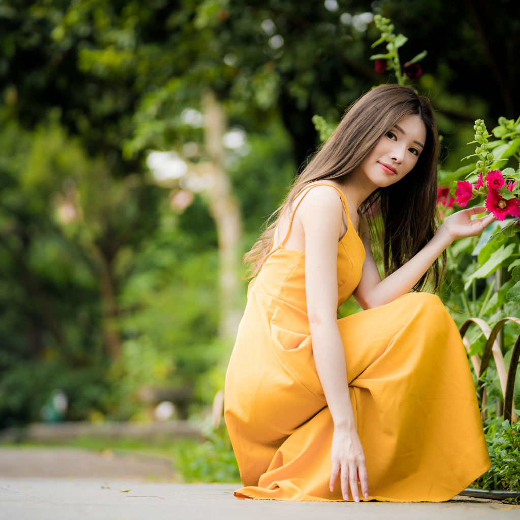Девушка в желтом платье сидит у цветка мальвы в парке