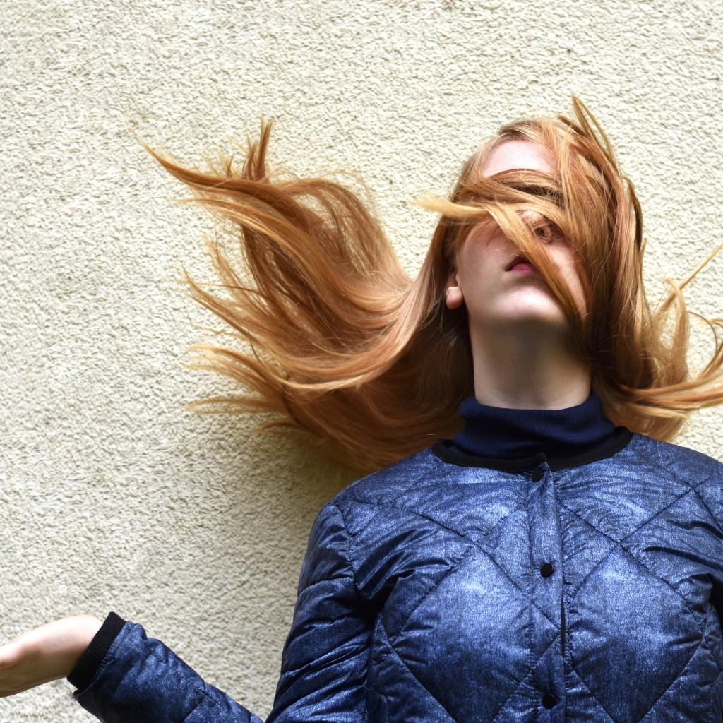 Девушка с волосами на лице стоит у стены