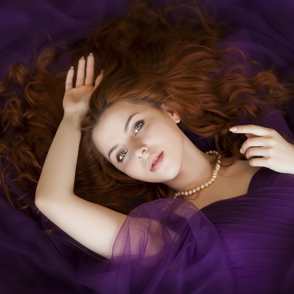 Рыжеволосая девушка в фиолетовом наряде лежит на полу