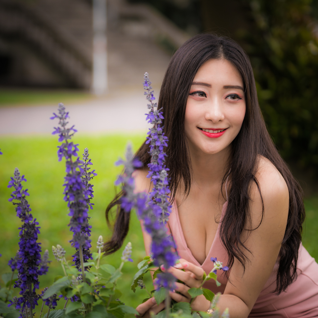 Улыбающаяся азиатка стоит у синих цветов 