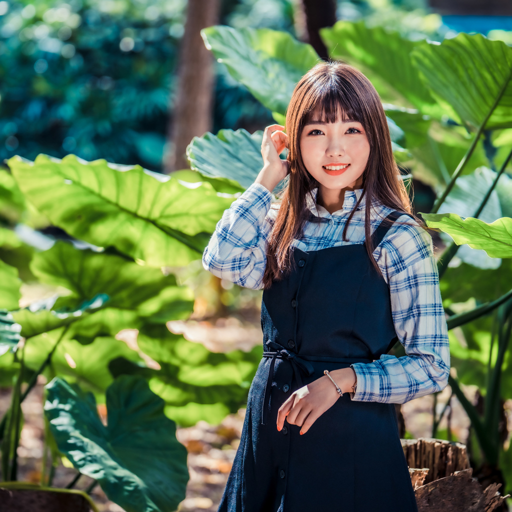 Улыбающаяся девушка азиатка в черном платье стоит в парке