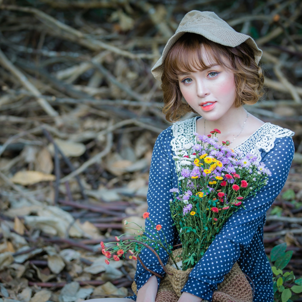 Молодая девушка азиатка с букетом цветов сидит на ветках