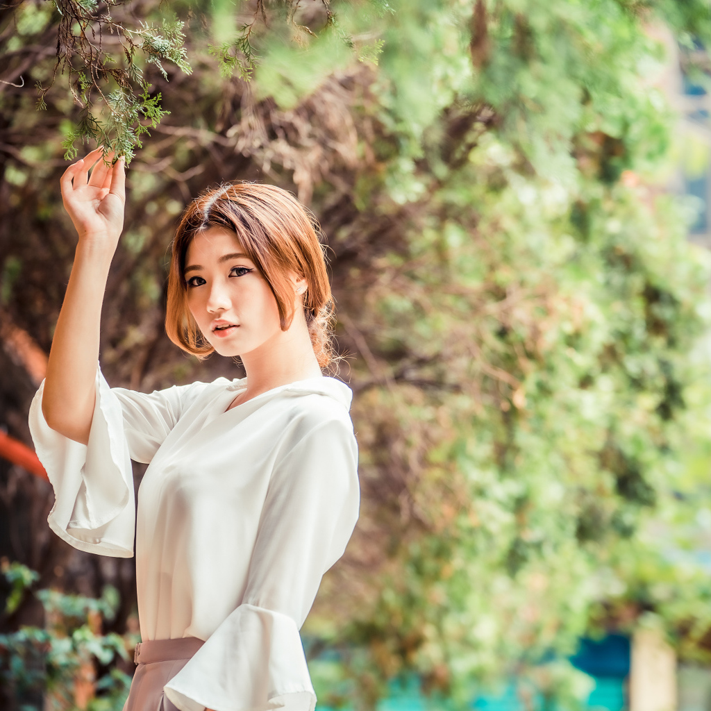 Молодая азиатка в белой блузке стоит у дерева 