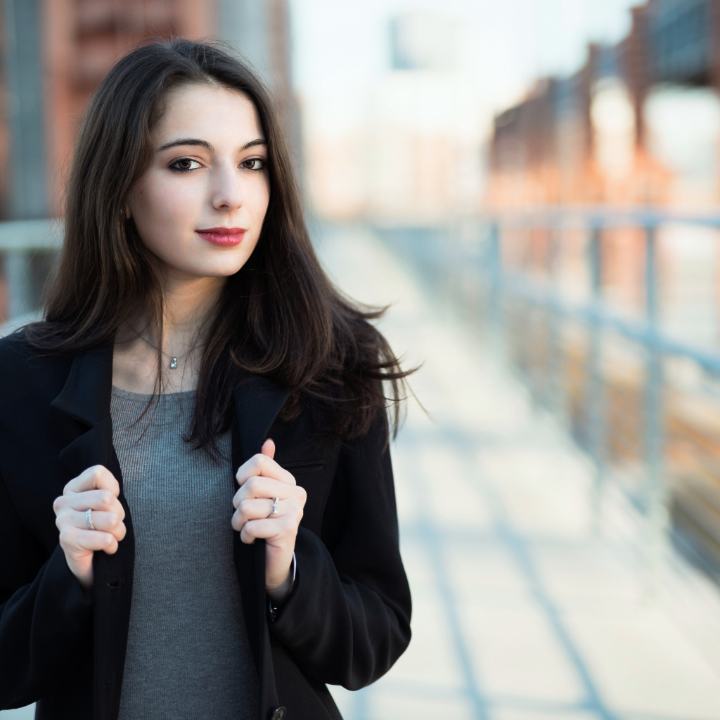 Молодая девушка в черном пальто стоит на мосту