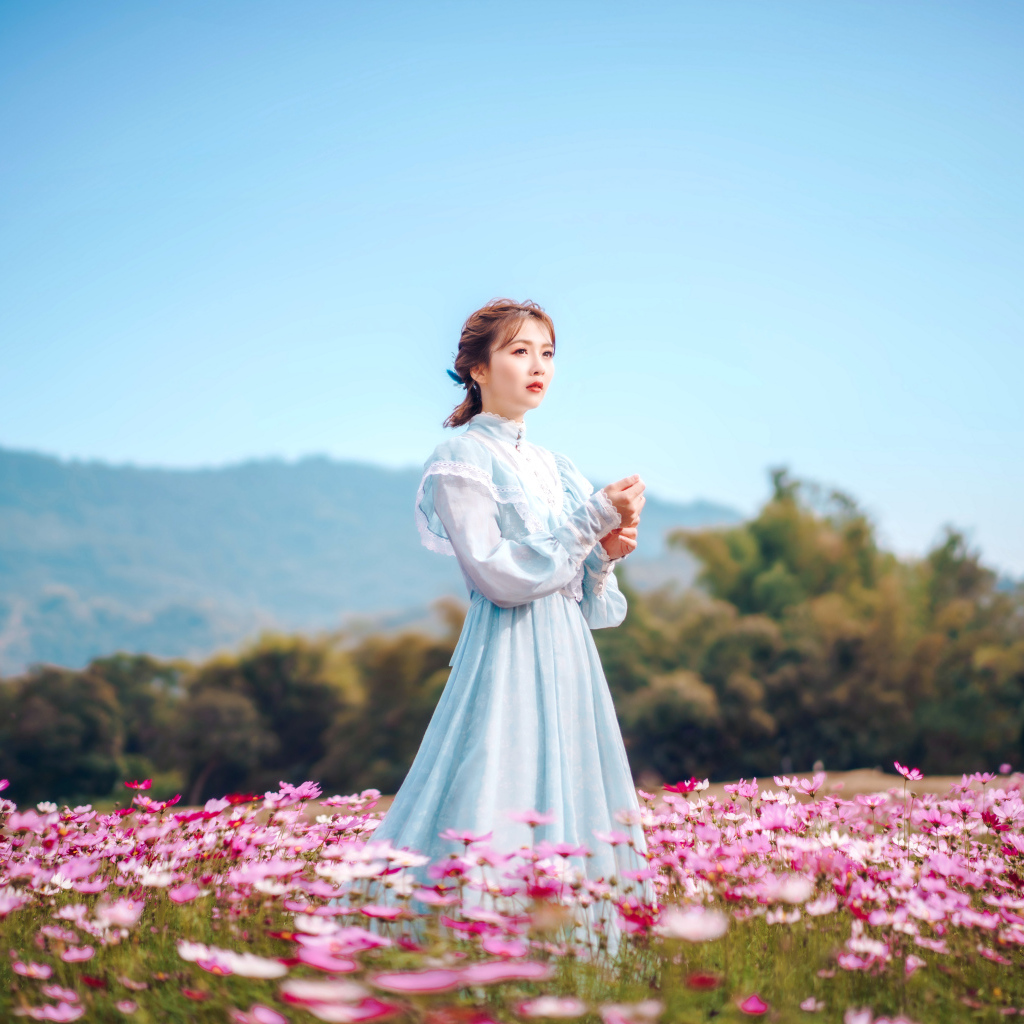 Девушка азиатка в красивом платье идет по полю с цветами космеи