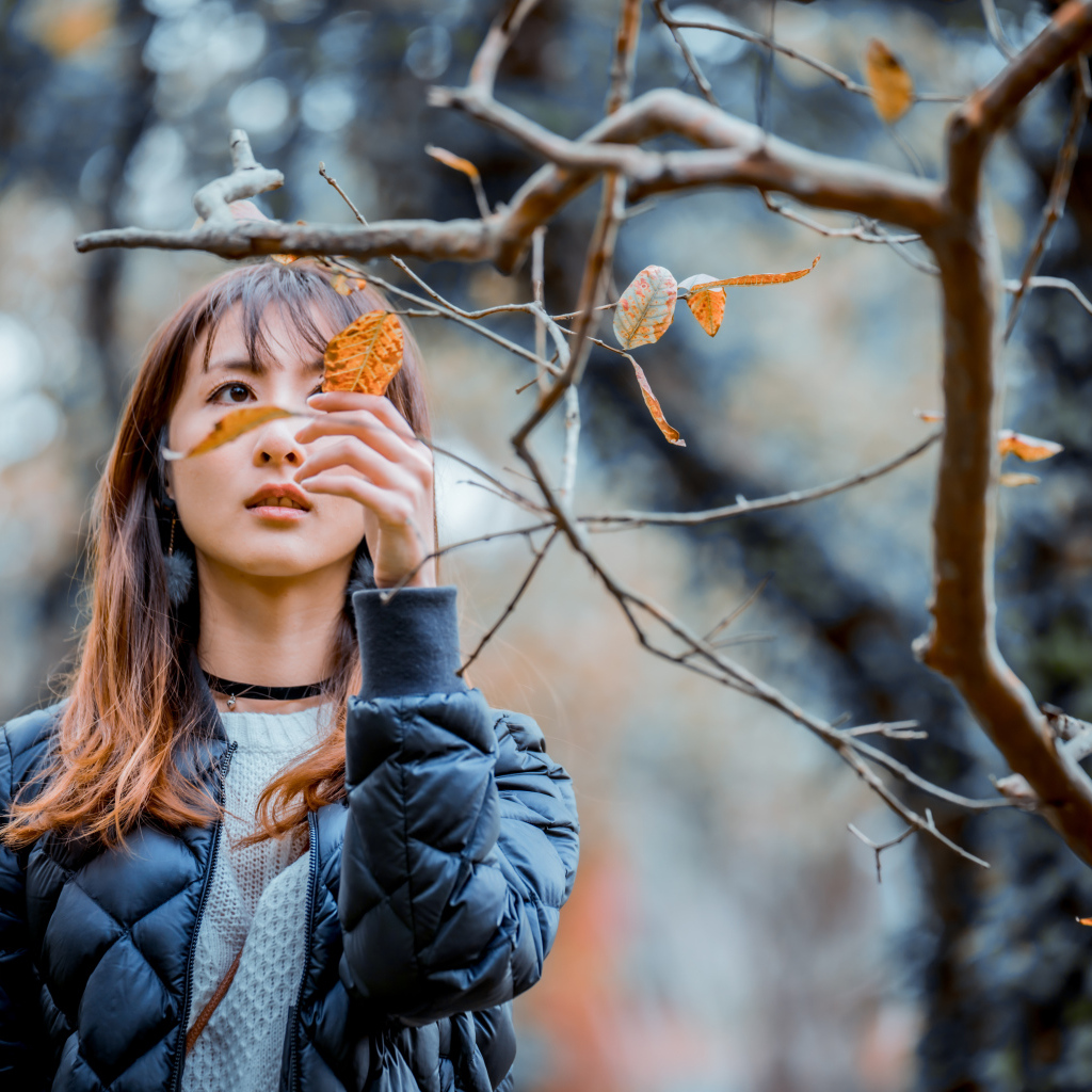 Девушка азиатка в черной куртке у дерева