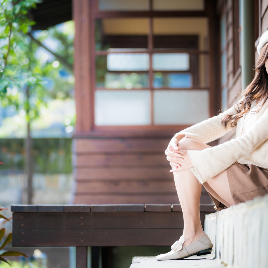 Девушка азиатка в свитере сидит на пороге 