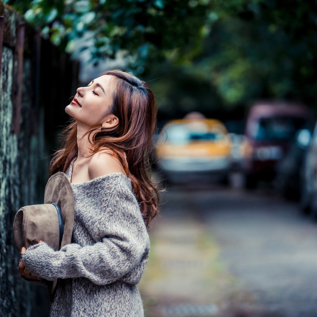Девушка азиатка в теплом свитере стоит у забора