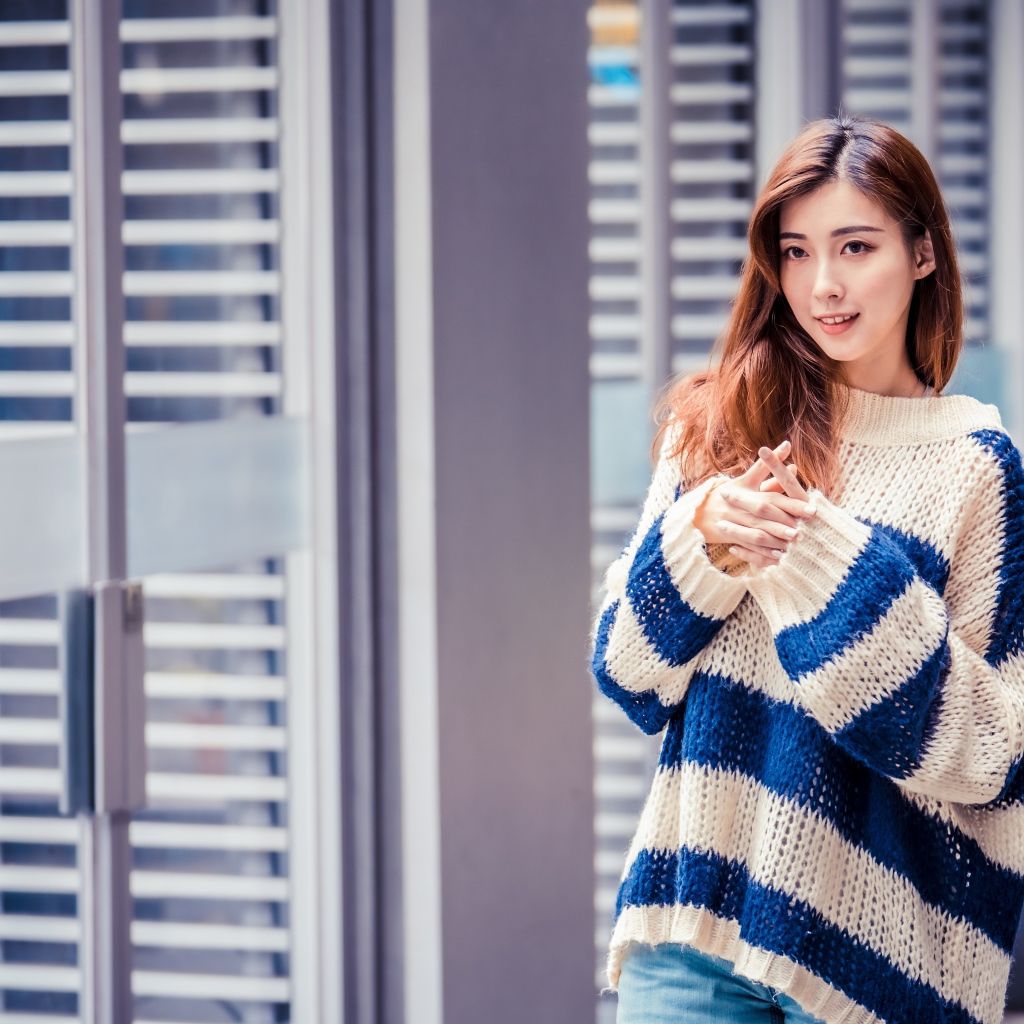 Девушка азиатка в теплом свитере стоит у окна