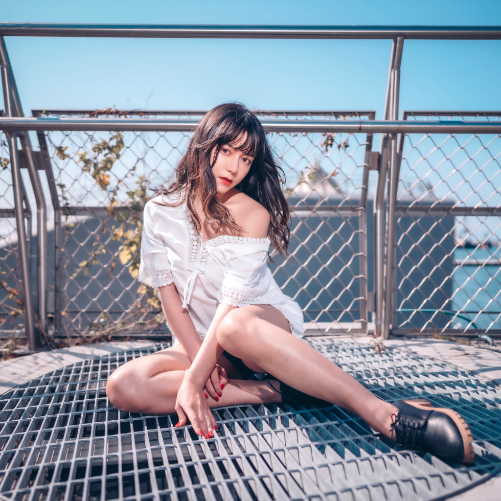 Девушка азиатка в белом наряде сидит на сетке