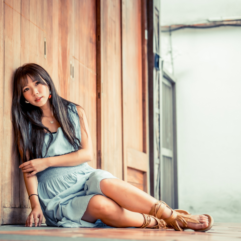 Девушка азиатка в платье сидит на полу у стены 