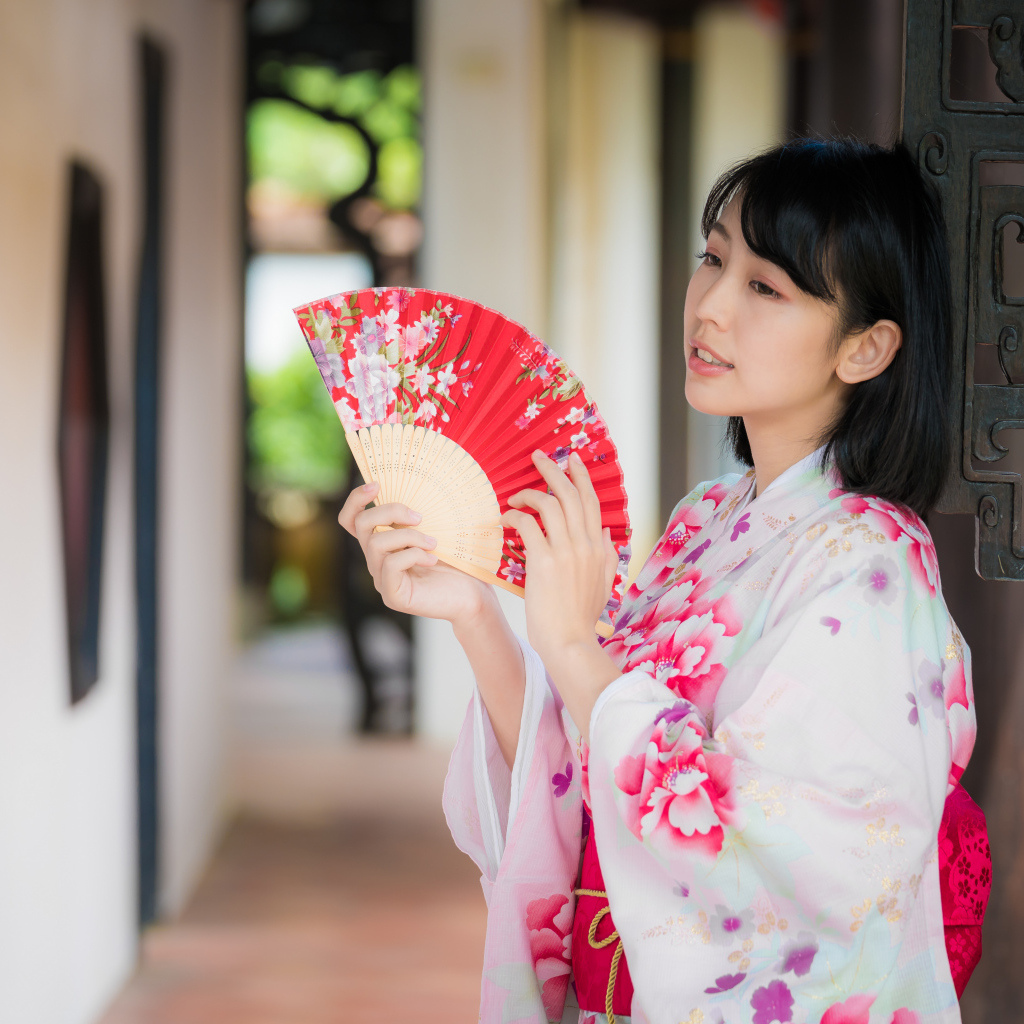 Девушка азиатка в кимоно с веером в руке стоит у ворот 
