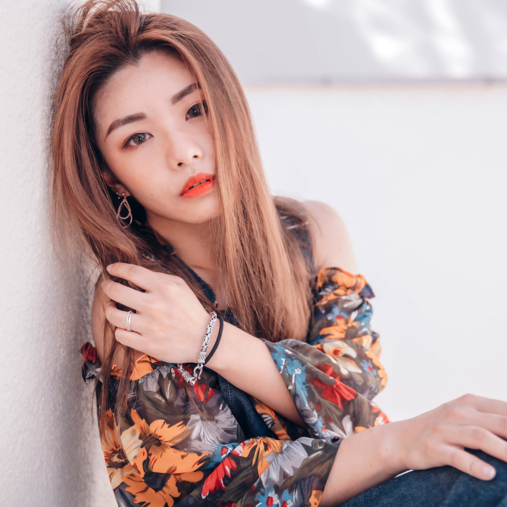 Девушка азиатка сидит на полу у стены 