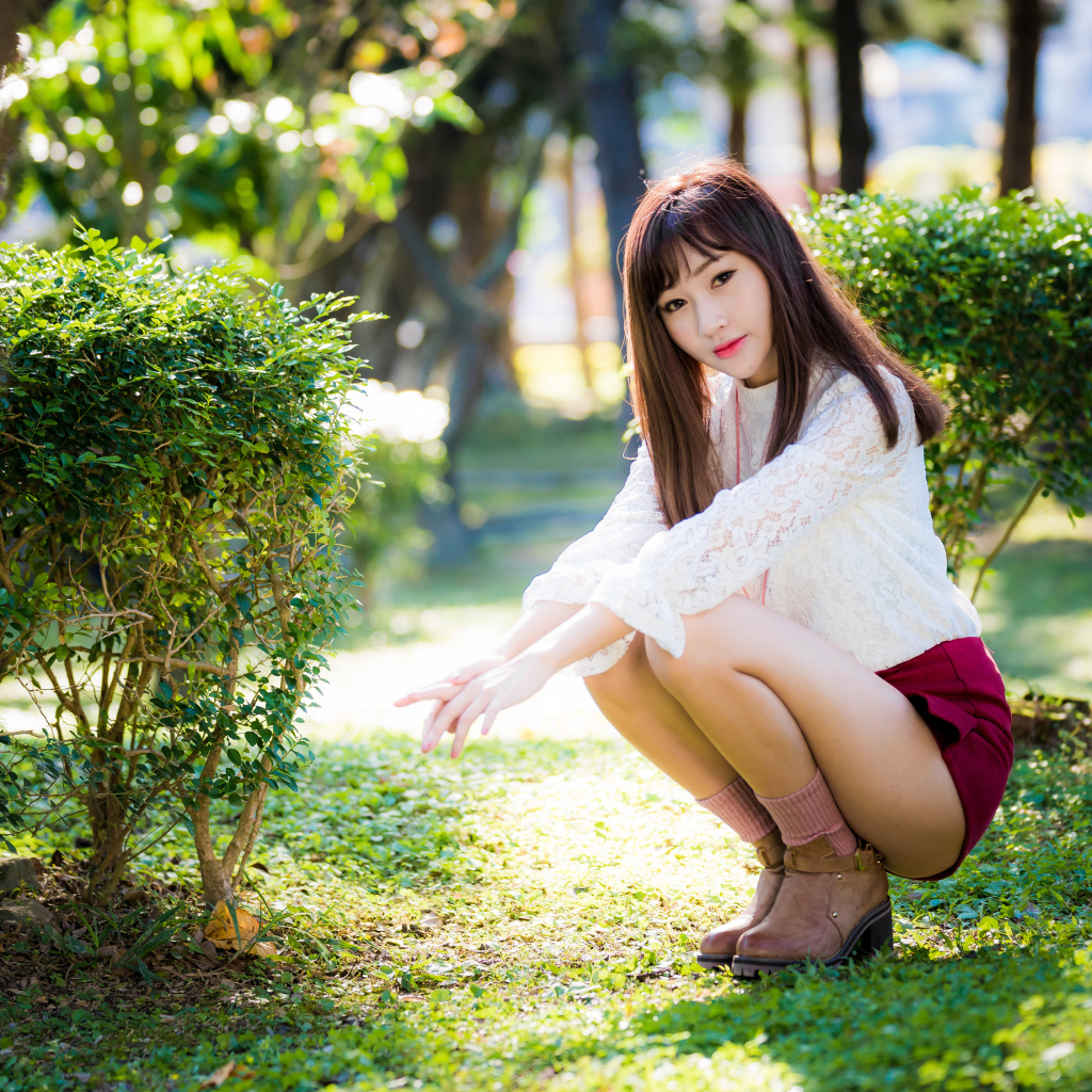 Девушка азиатка сидит на корточках в парке