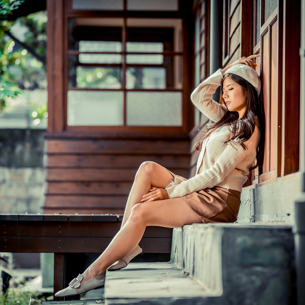 Девушка азиатка с закрытыми глазами сидит на ступеньках дома 