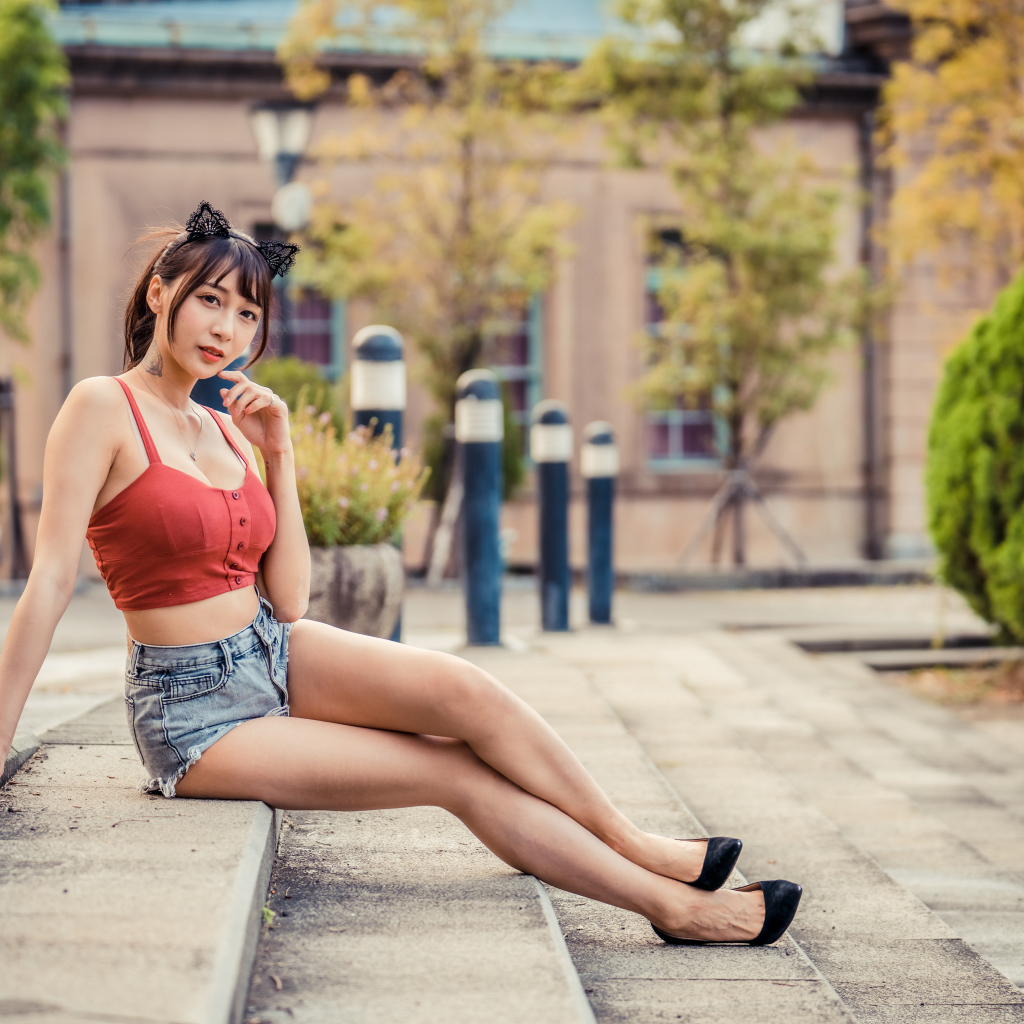 Азиатка в шортах сидит на ступенях 