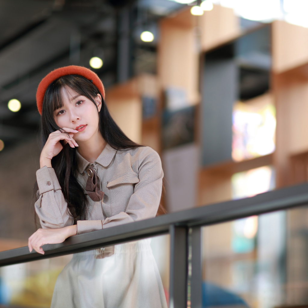 Азиатка в сером платье стоит у перил 