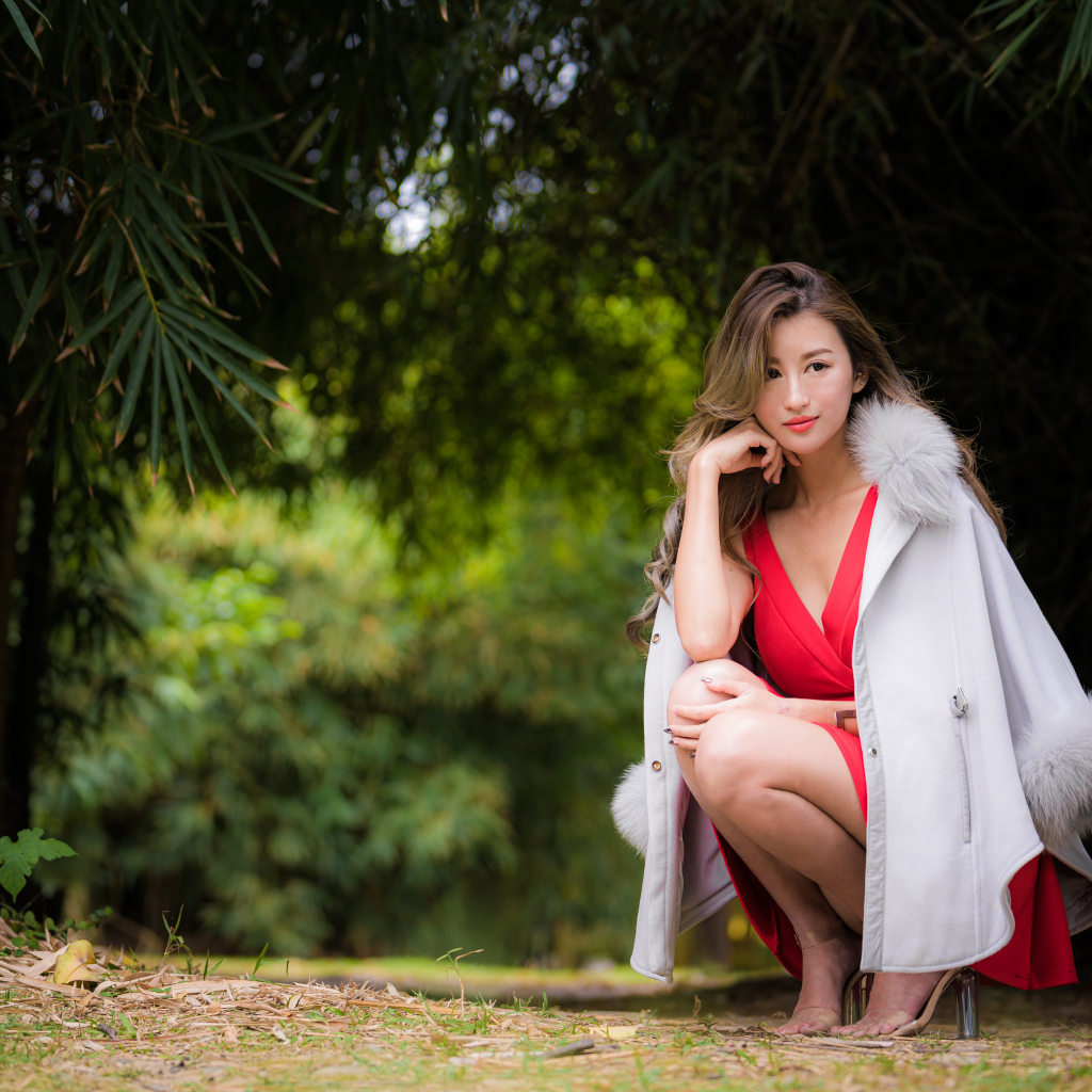 Азиатка в красном платье сидит в парке 