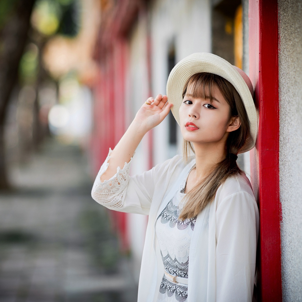 Красивая азиатка в шляпе стоит у стены