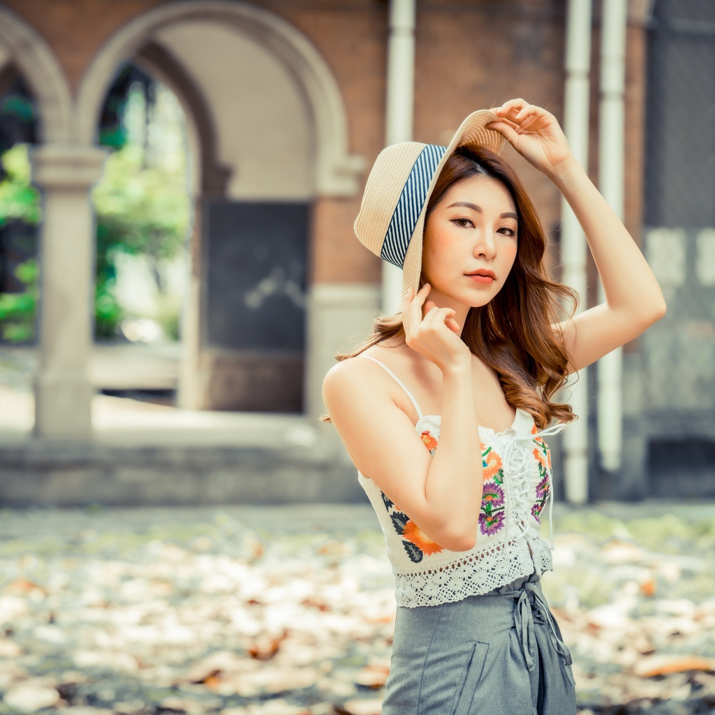 Красивая девушка азиатка в шляпе стоит в парке 