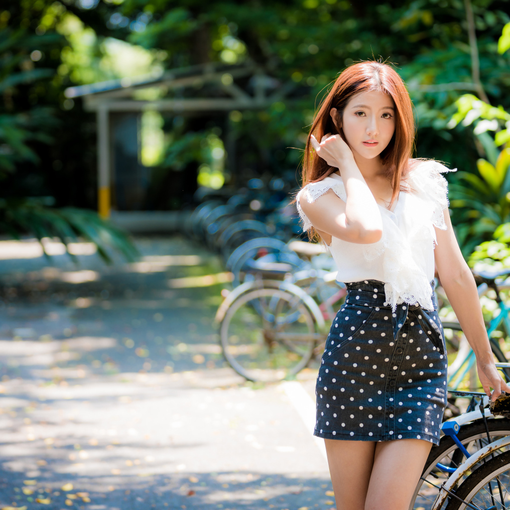 Красивая девушка азиатка в юбке в горох стоит у велосипеда 
