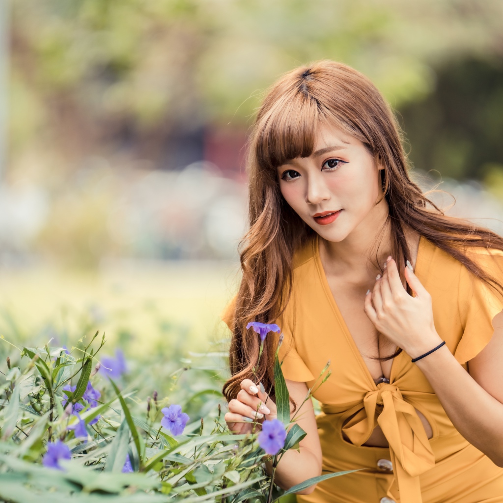 Красивая девушка азиатка в желтом платье у фиолетовых цветов 