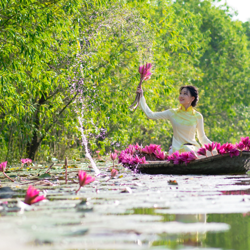 Красивая девушка азиатка на лодке рвет цветы лотоса в реке