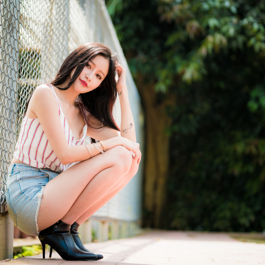 Красивая девушка азиатка сидит у железной сетки