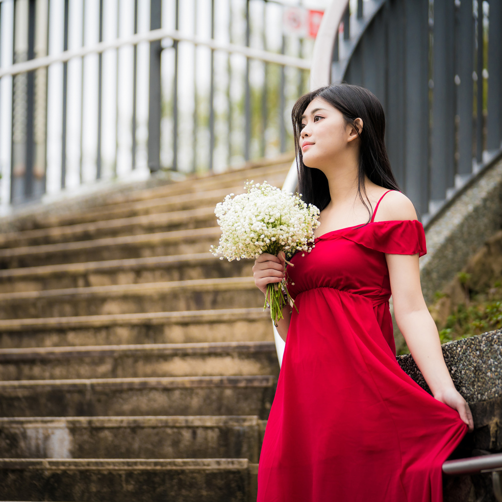 Красивая азиатка в красном платье стоит на ступеньках с букетом ландышей