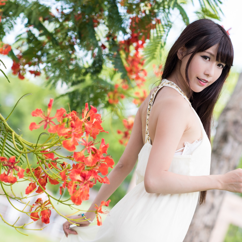 Красивая девушка азиатка в красном платье у дерева с цветами