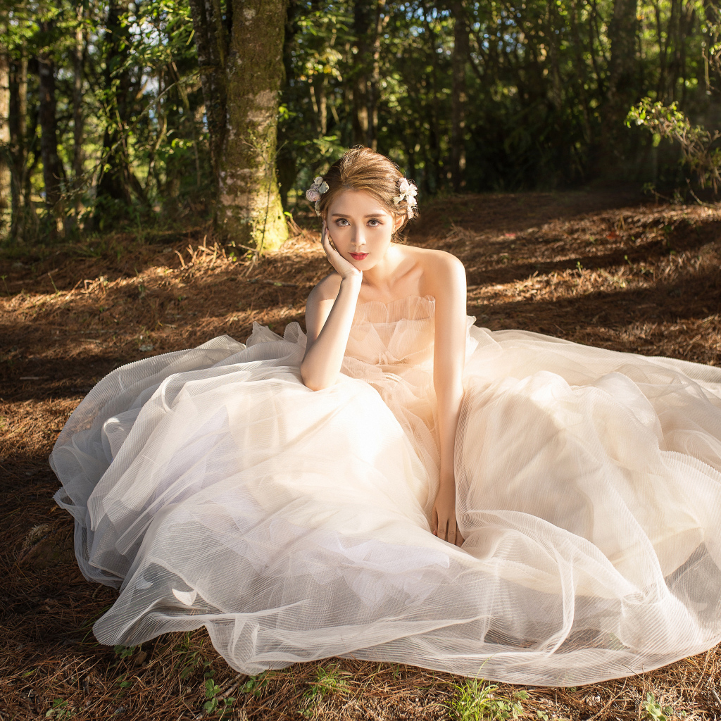 Красивая девушка азиатка в белом свадебном платье сидит на земле