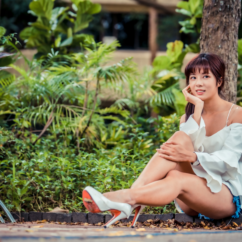 Красивая девушка азиатка сидит на земле в парке 